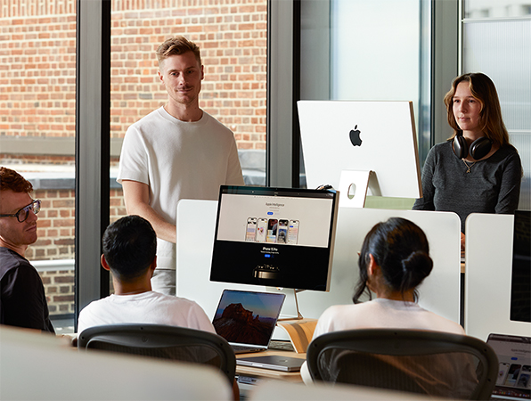 Cinq membres de l’équipe Apple discutant autour de leurs bureaux.