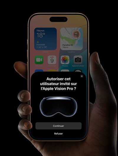 Une main tient un iPhone. L’écran de l’iPhone affiche une fenêtre avec le message « Autoriser cet utilisateur invité sur l’Apple Vision Pro ? » et les boutons « Continuer » et « Refuser. »