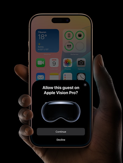 A hand holding an iPhone. The iPhone's screen displays a window with the message, "Allow this guest on Apple Vision Pro?" with buttons labeled "Continue" and "Decline."