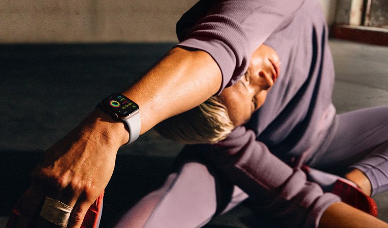 Apple Watch Series 10을 착용한 상태로 바닥에 앉아 팔을 다리 끝까지 뻗어 스트레칭하는 여성의 모습. Apple Watch 화면에는 운동 앱, 정리 운동, 활동, 활동 링이 표시되어 있습니다.