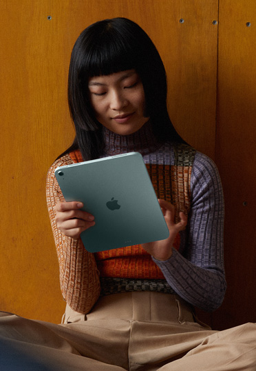Một sinh viên đang ngồi trên sàn, dựa lưng vào tường. Cô ấy đang cầm một chiếc iPad.
